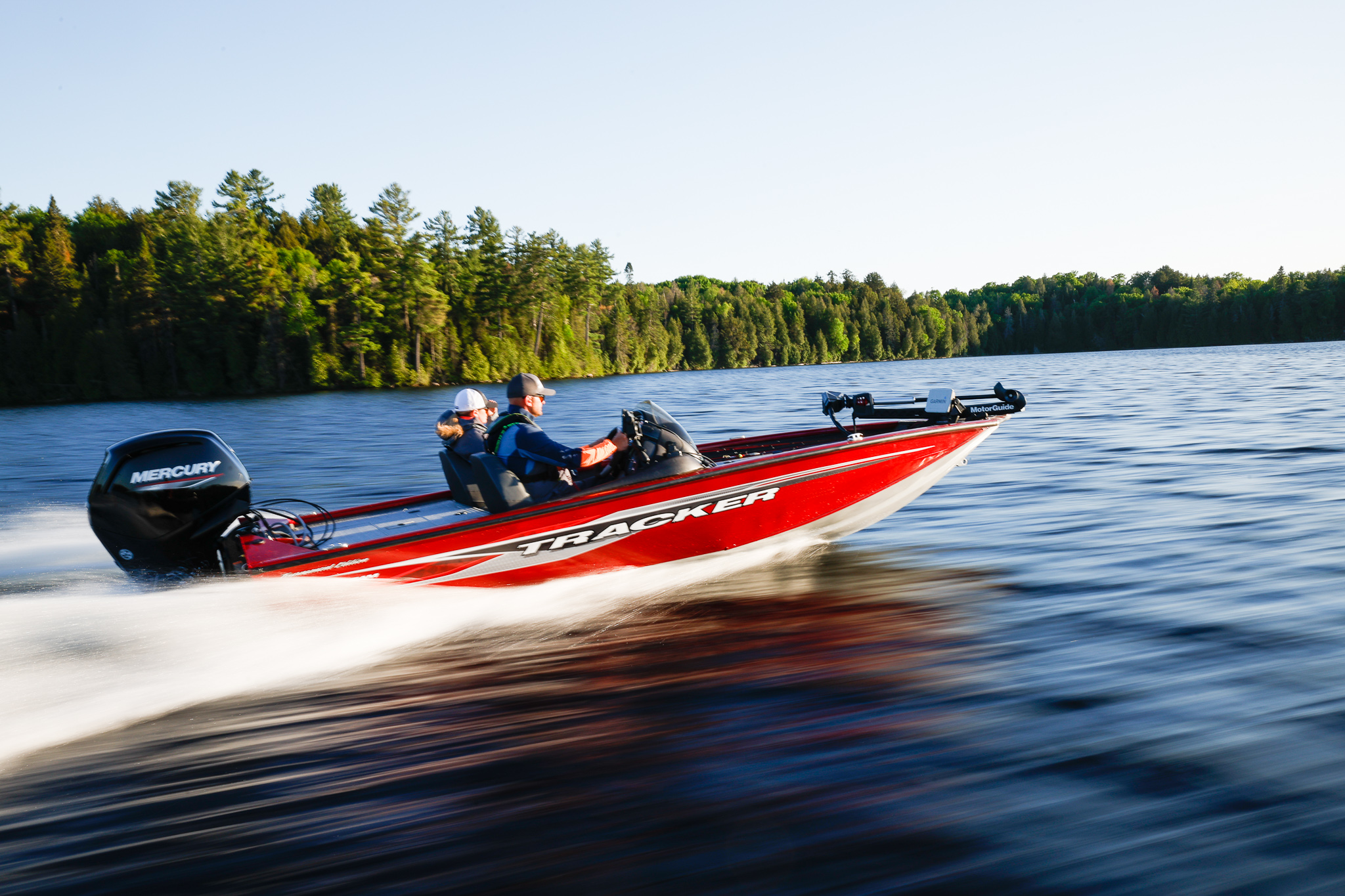 A red fishing boat moving quickly with two people on board. 