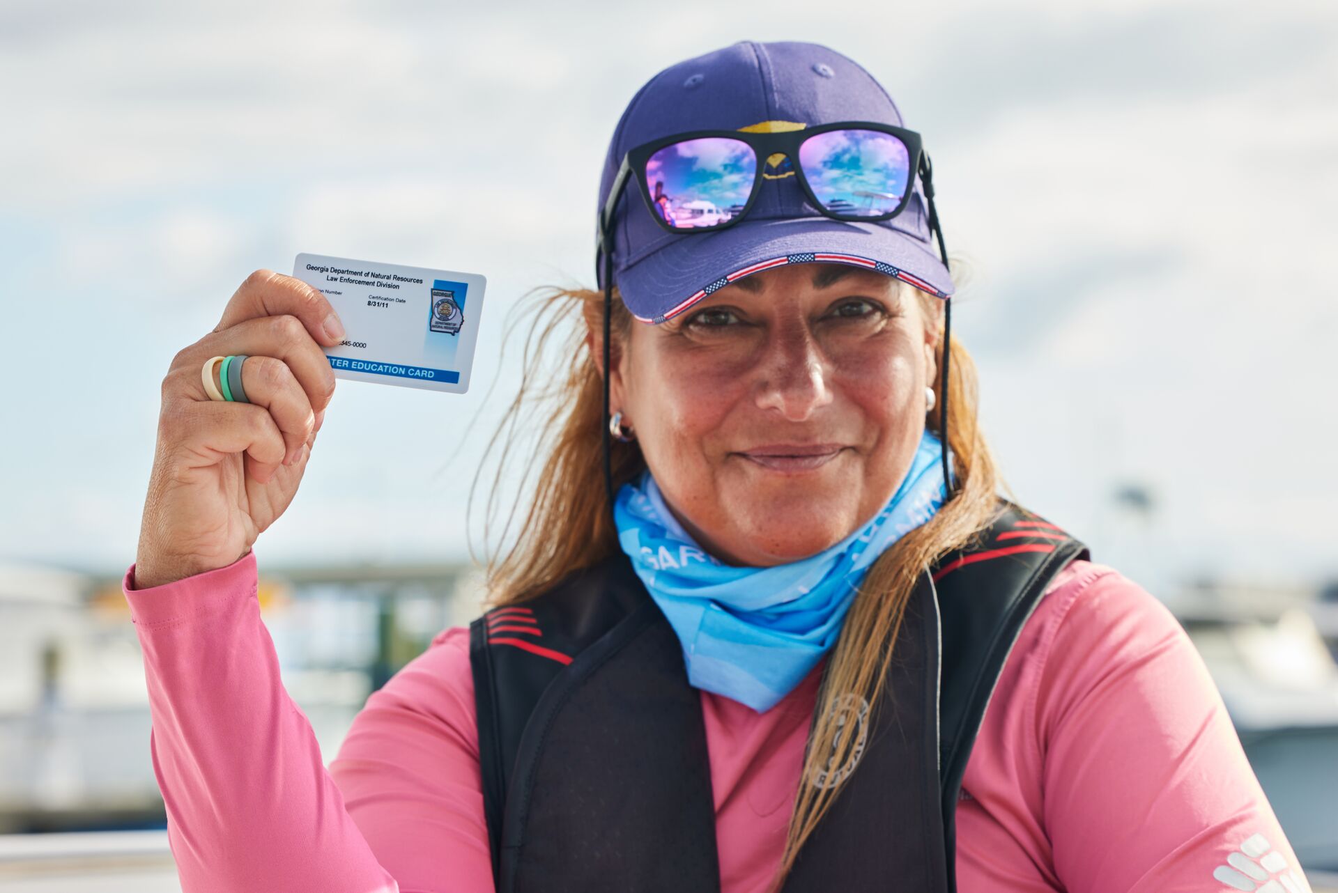 A woman holds a boater card, smiles, wears a life jacket, reduce boating accident statistics with education concept. 