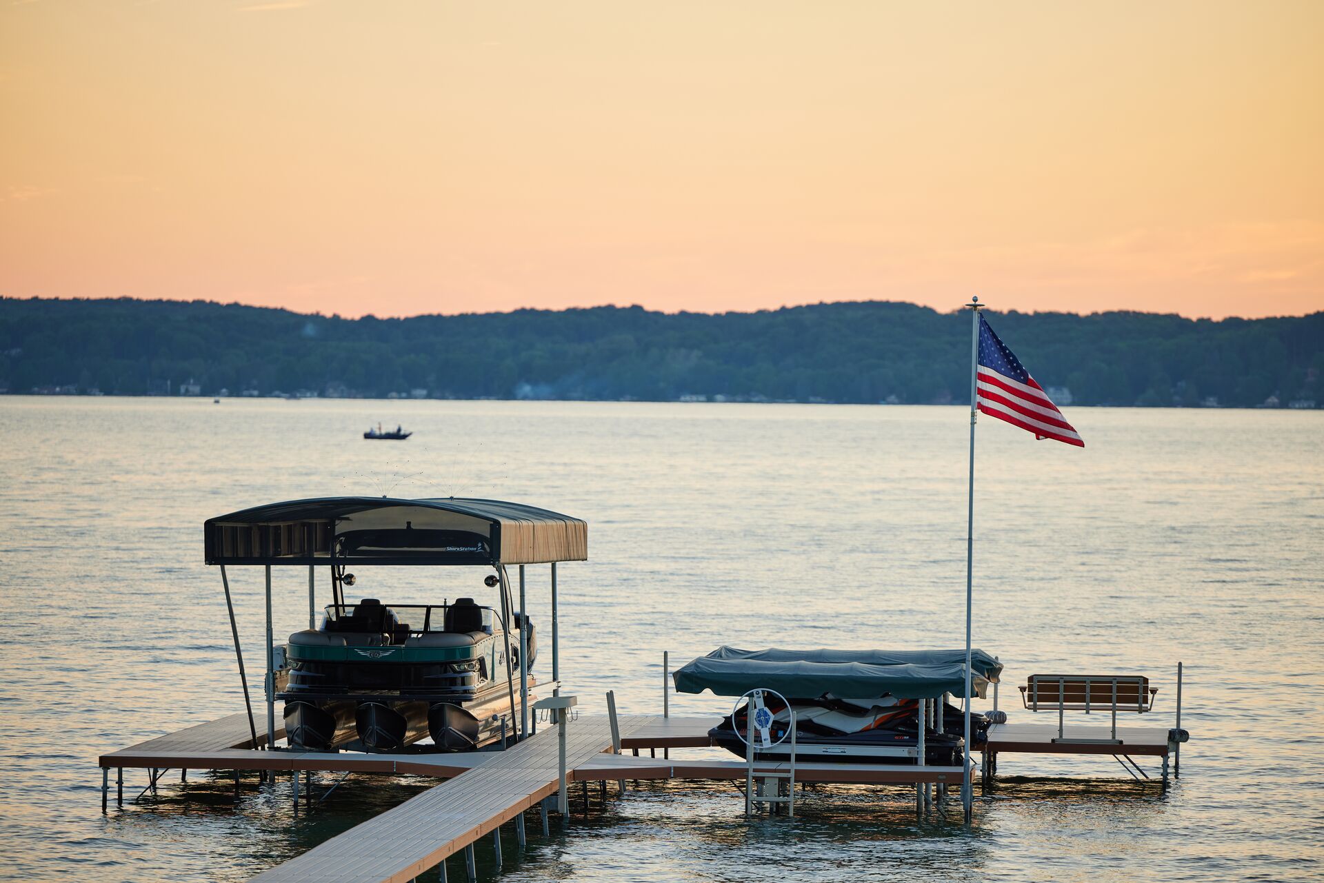 A pontoon boat at a dock out of the water with a U.S. flag flying nearby. 