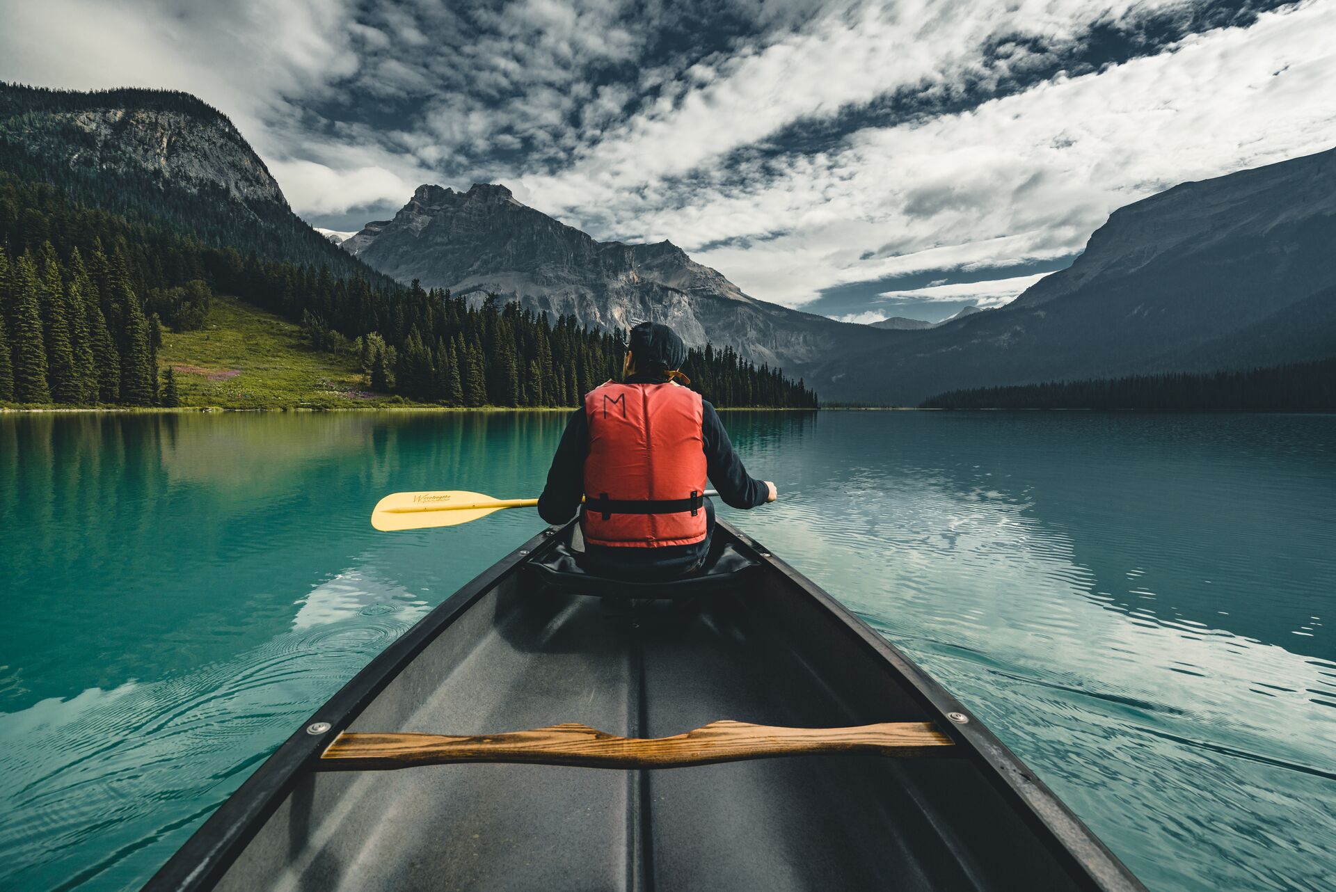 A person at the front of a canoe wearing a lifejacket on water in the mountains, paddlesports concept. 