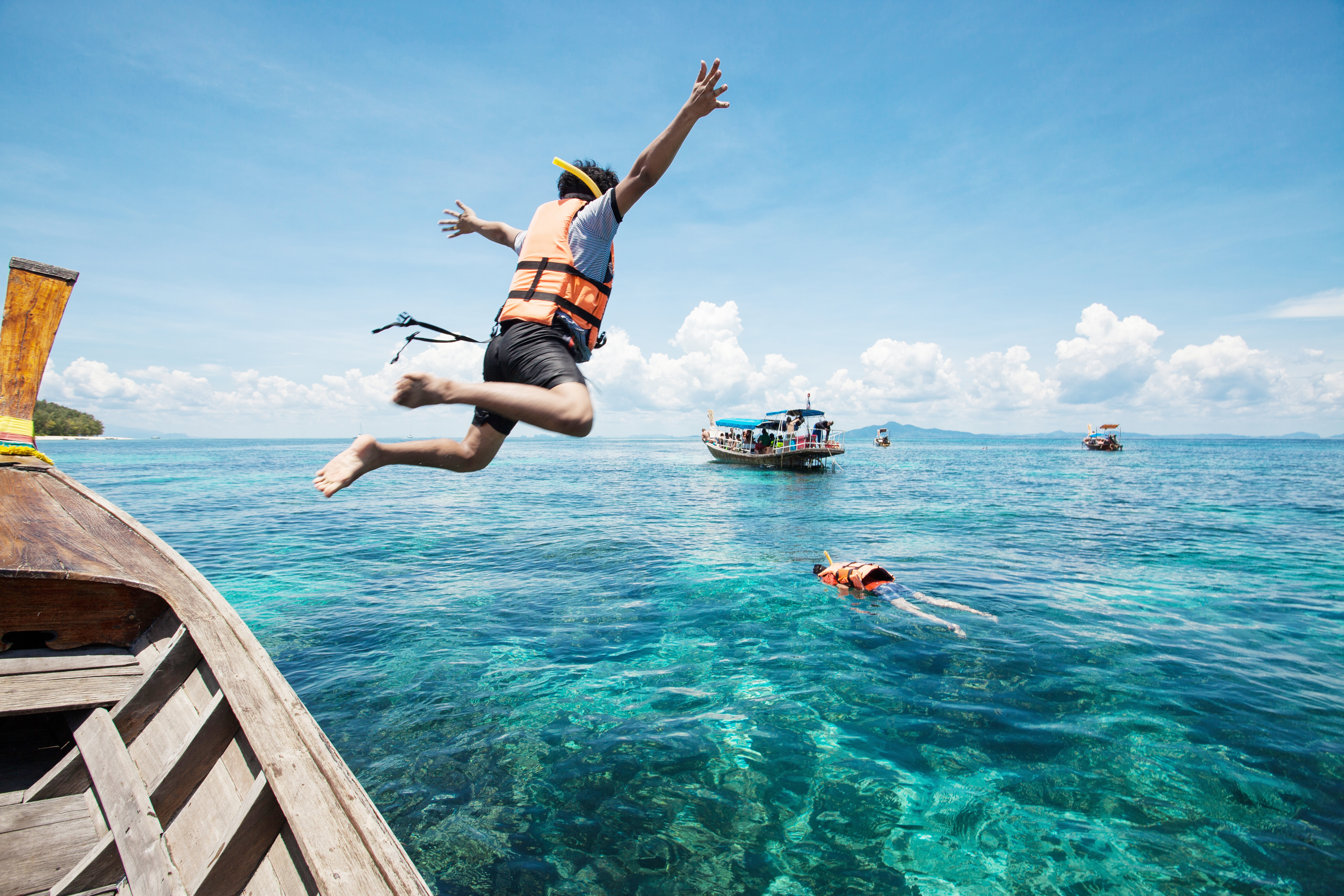 People jumping from a boat while wearing life jackets. 