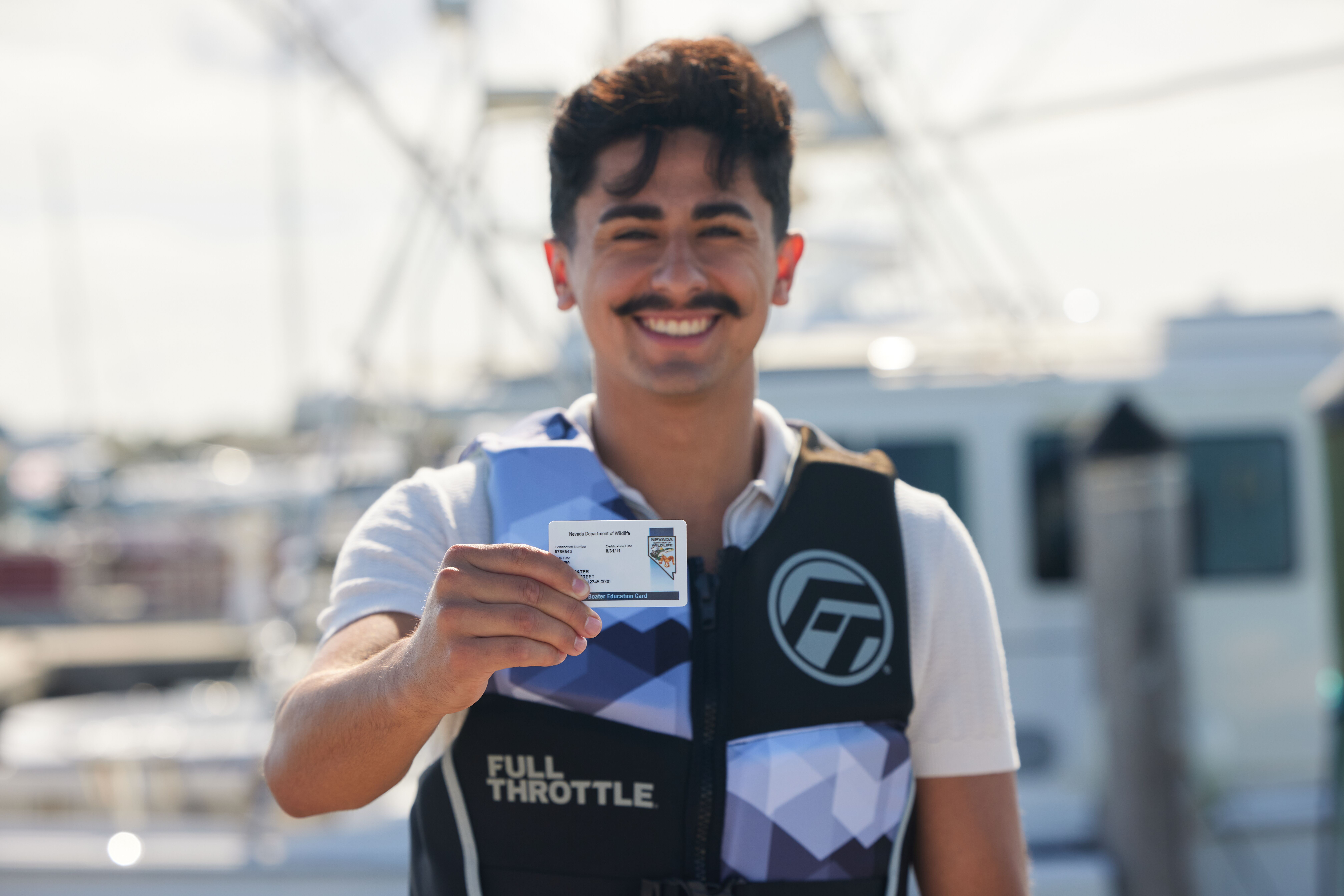 A smiling man wearing a life jacket and holding a boater safety card, using boat ramps safely concept. 