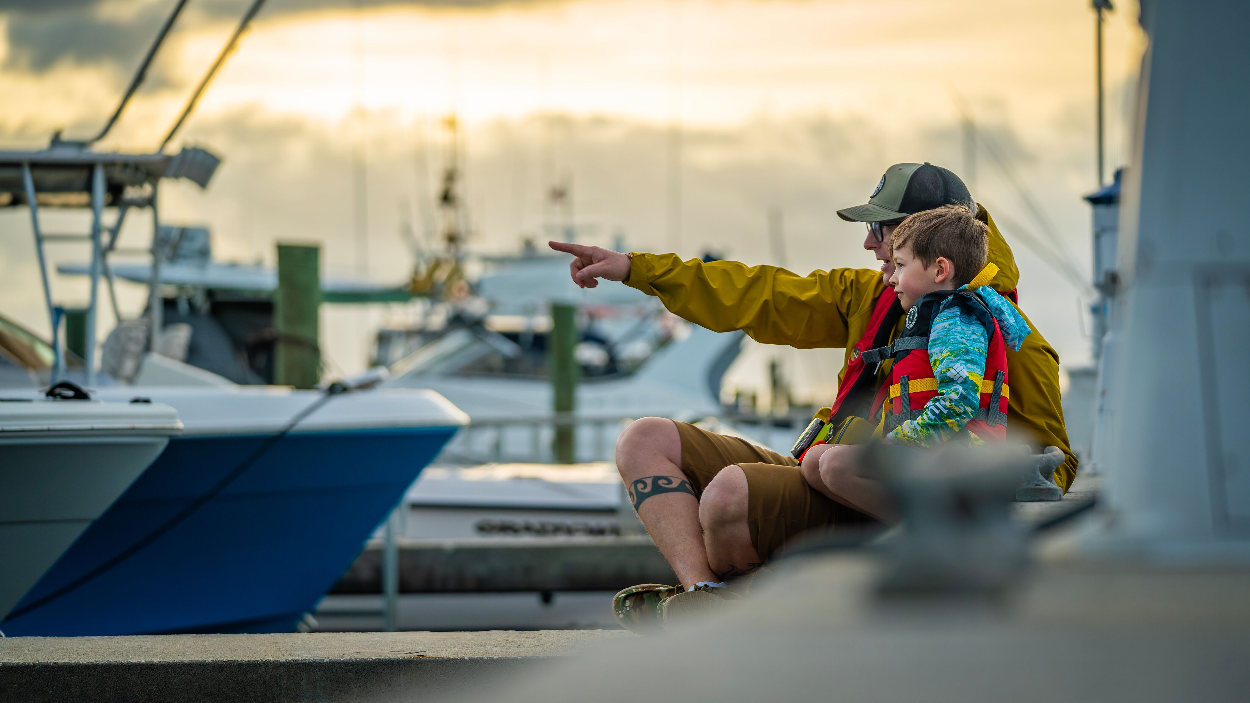 A man and a boy wait on a dock pointing at something in the distance, using boat ramps concept. 