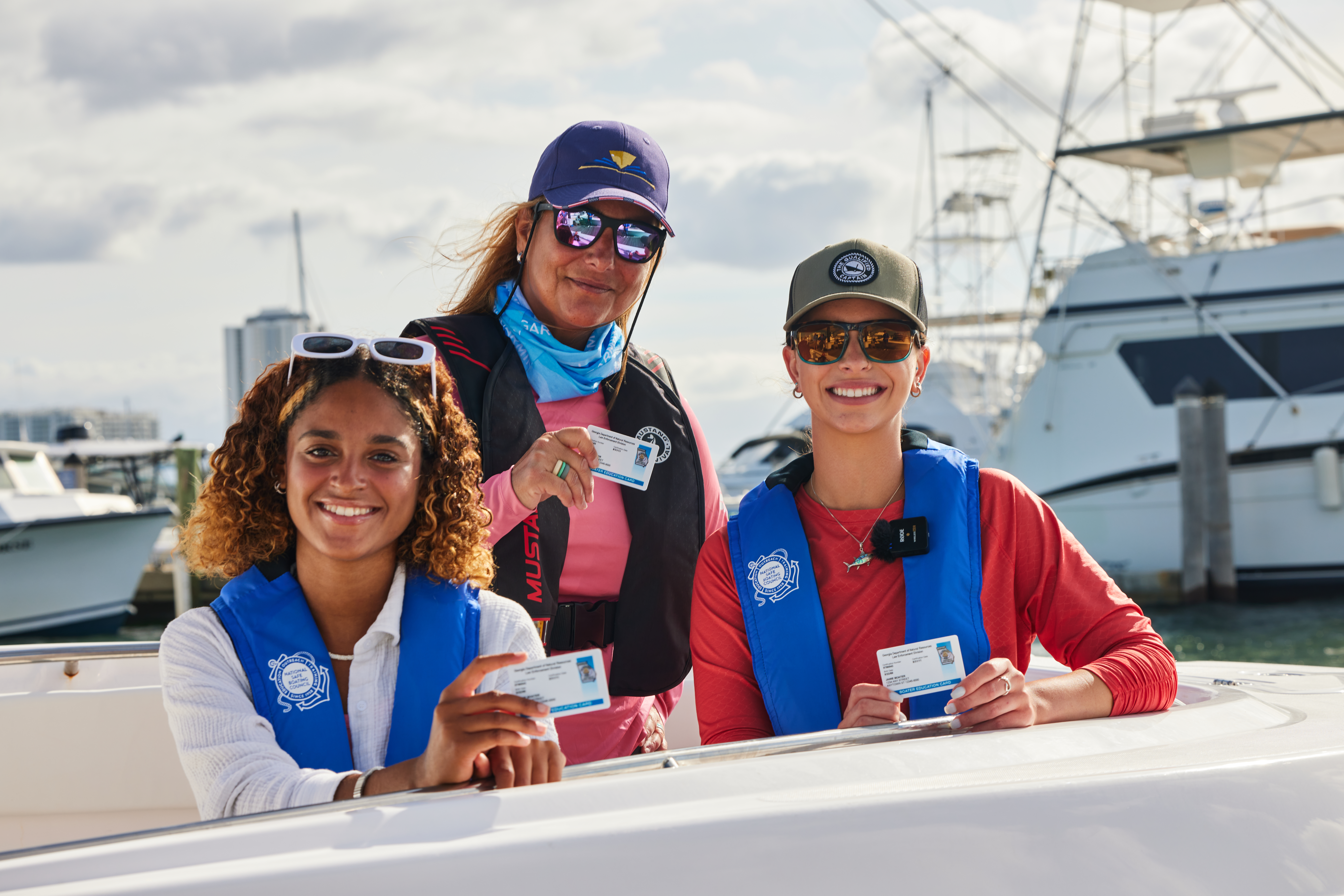 Three women wearing lifejackets on a boat while holding boater education cards, PWC safety education concept. 