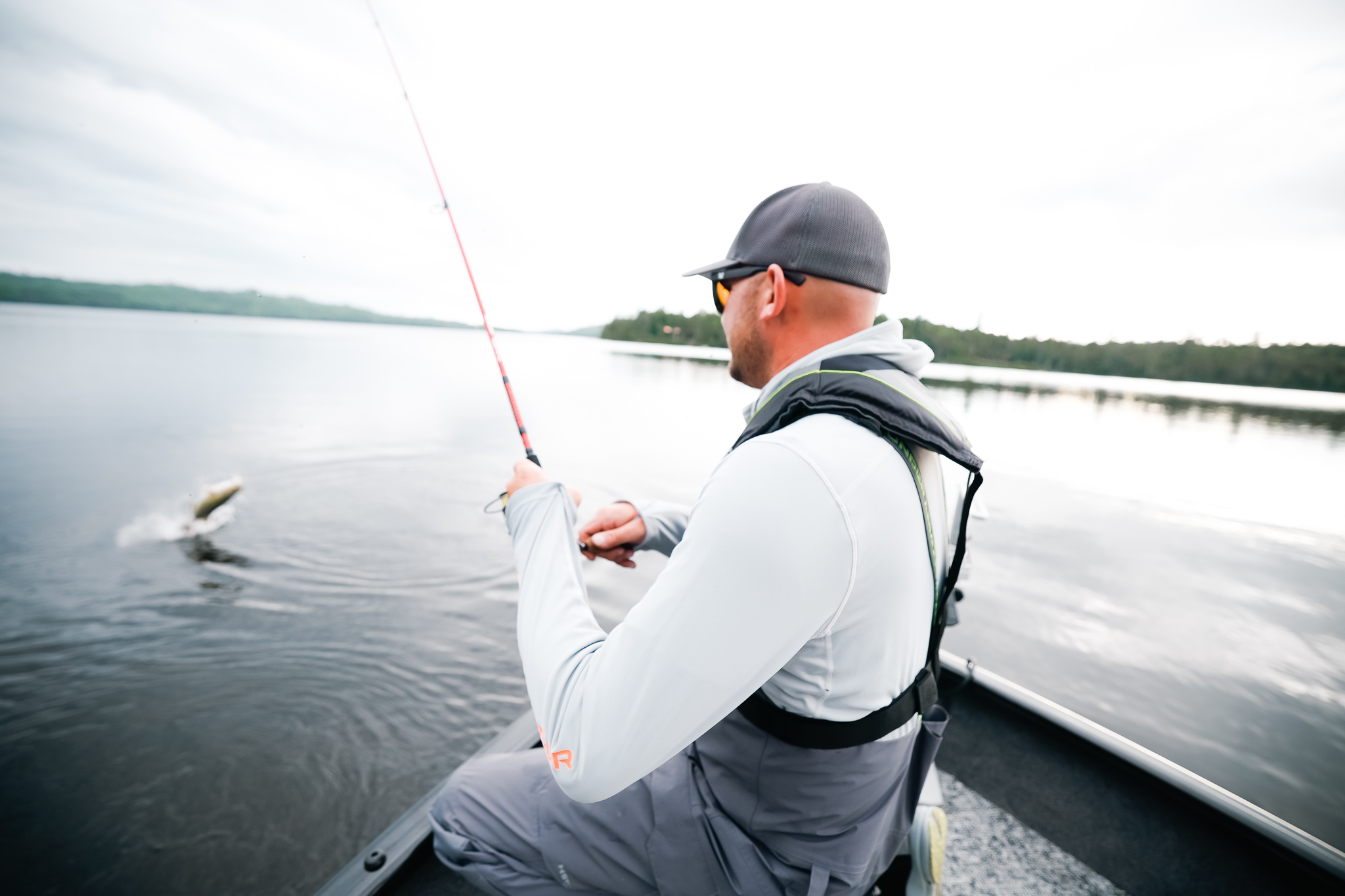 A man on a fishing boat handling a fishing rod to reel in a bass fish, fishing safely from a boat concept. 