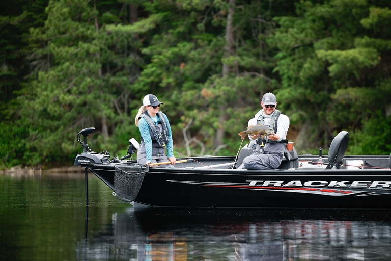 A man holding a bass fish while with a woman on a boat. 