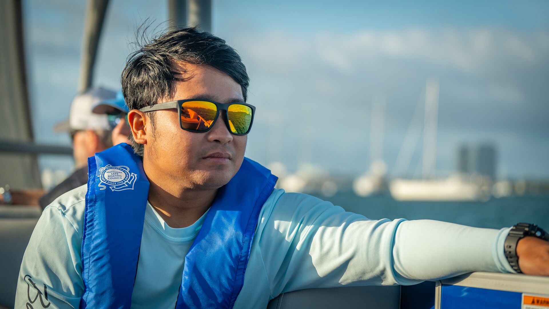 A man wearing sunglasses and a blue life jacket on a boat. 