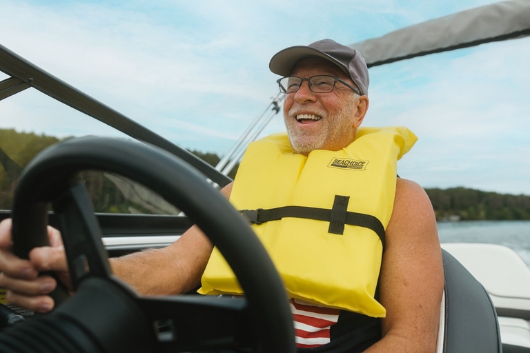 A smiling man steers a boat while wearing a yellow Type 2 life jacket. 