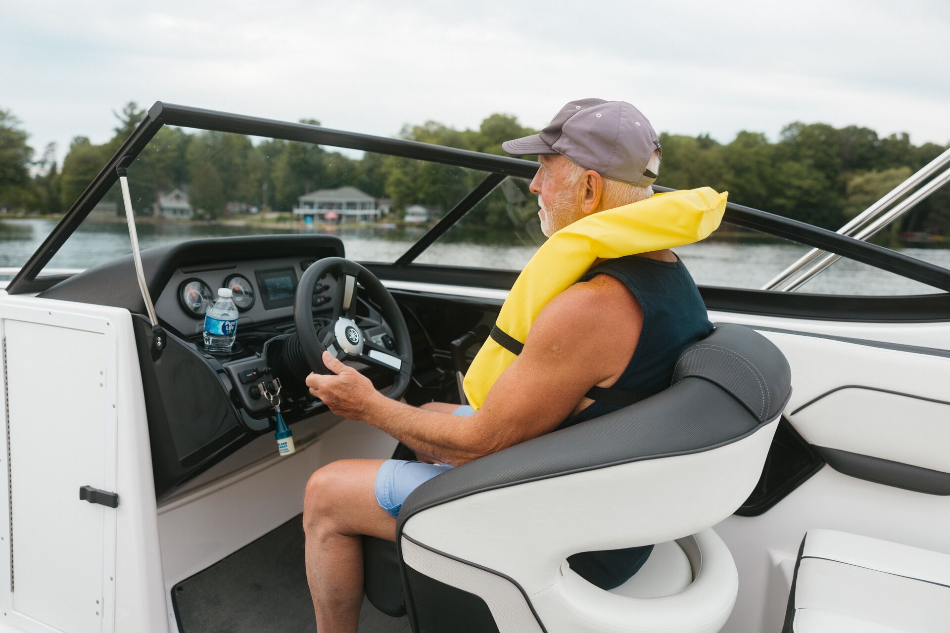 A man in a yellow lifejacket at the helm of a boat. 