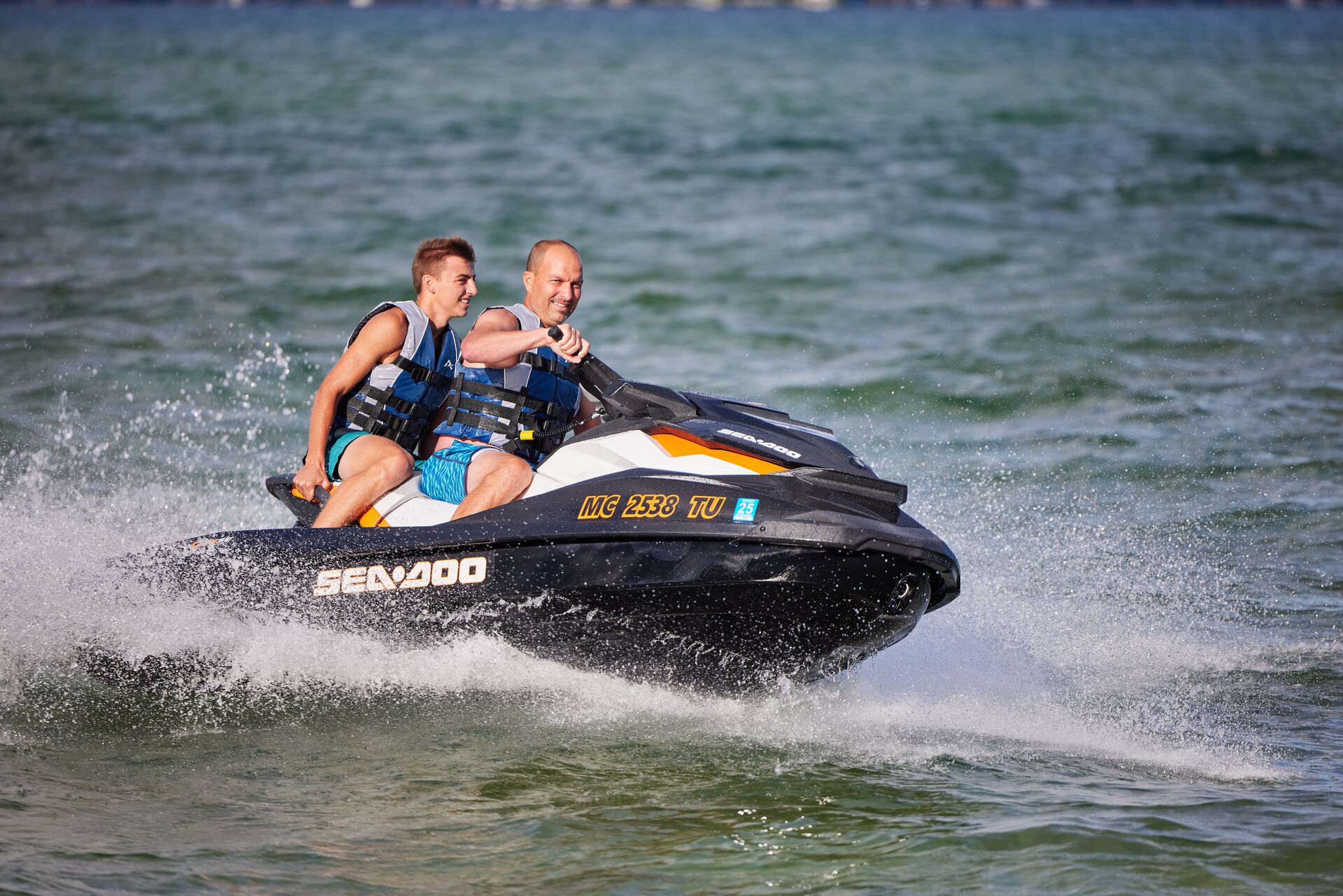 Two guys on a jet ski wearing life jackets. 