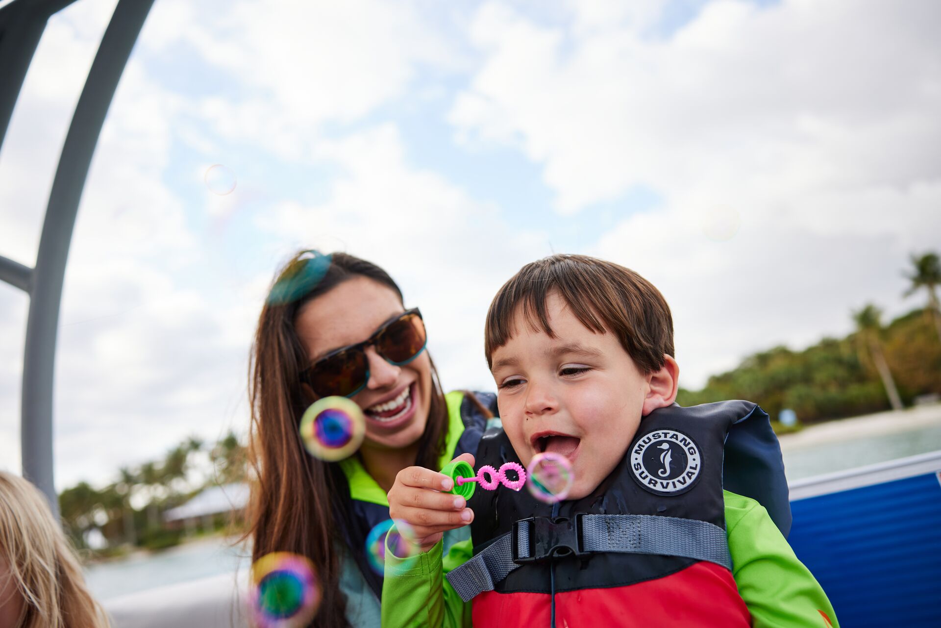 A child and woman wear a personal flotation device on a boat while blowing bubbles