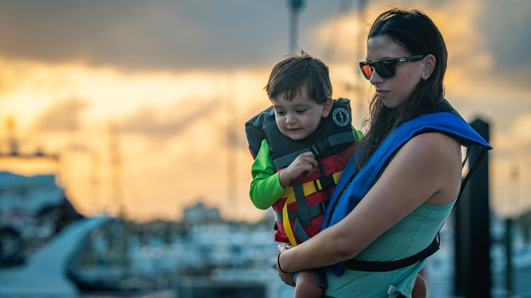 A woman and child on a dock looking down while wearing life jackets. 