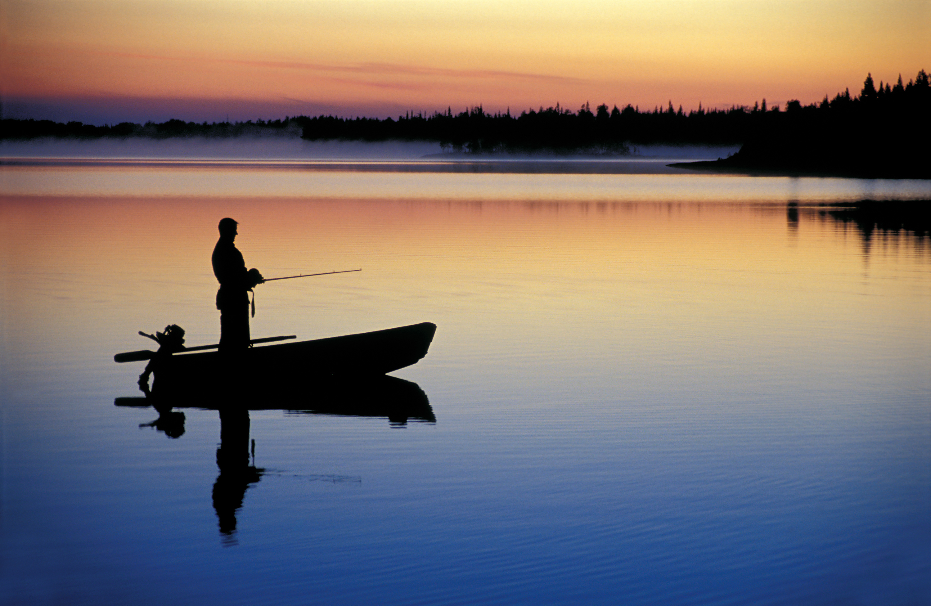 A silhouetted person in a fishing boat with a line in the water. 