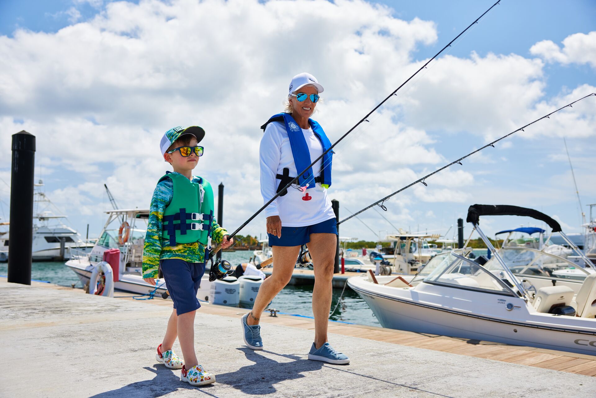 A woman and a boy walk on a dock with fishing poles, using fish and ski boats concept. 