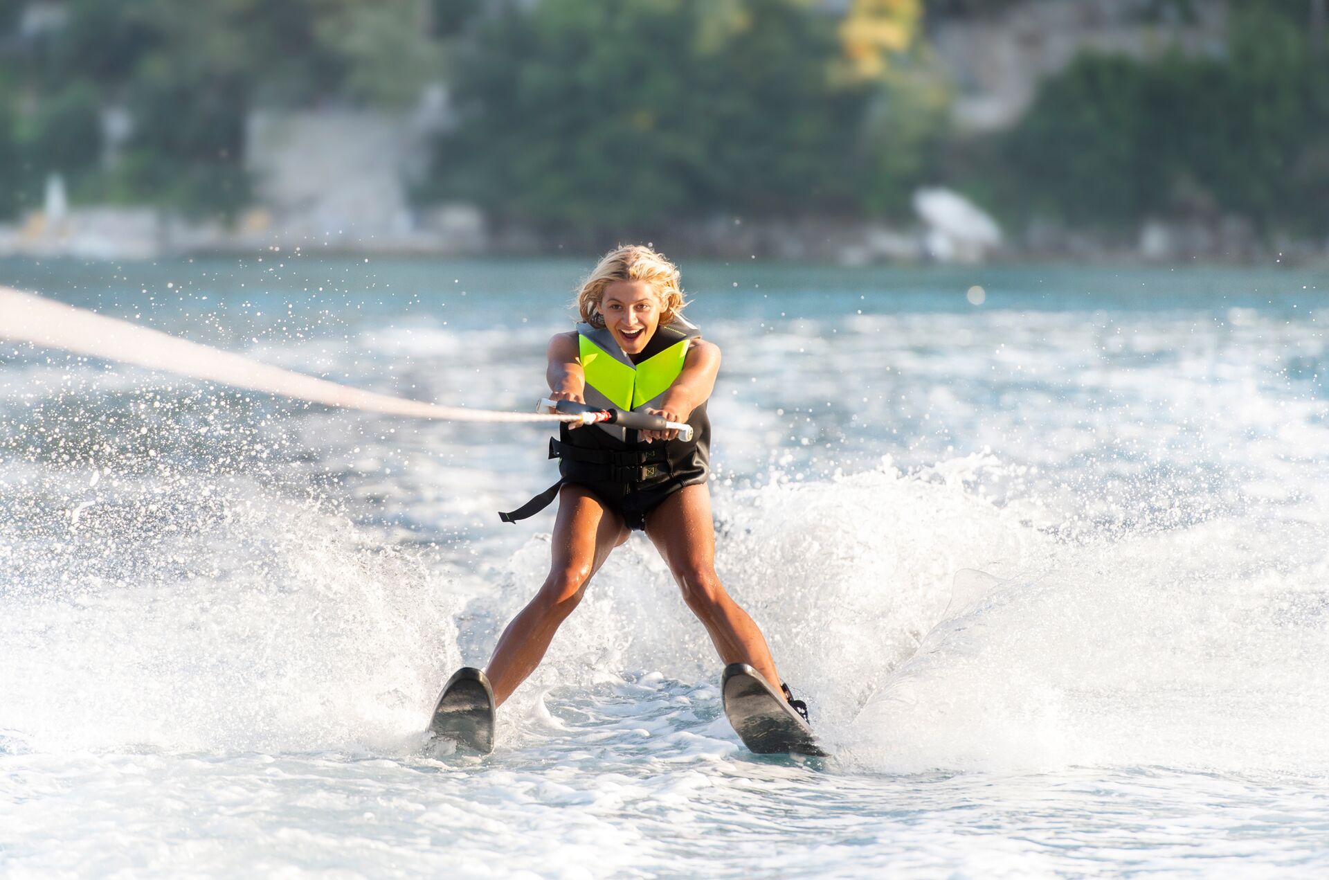 A girl smiles and wears a life jacket while on water skis.