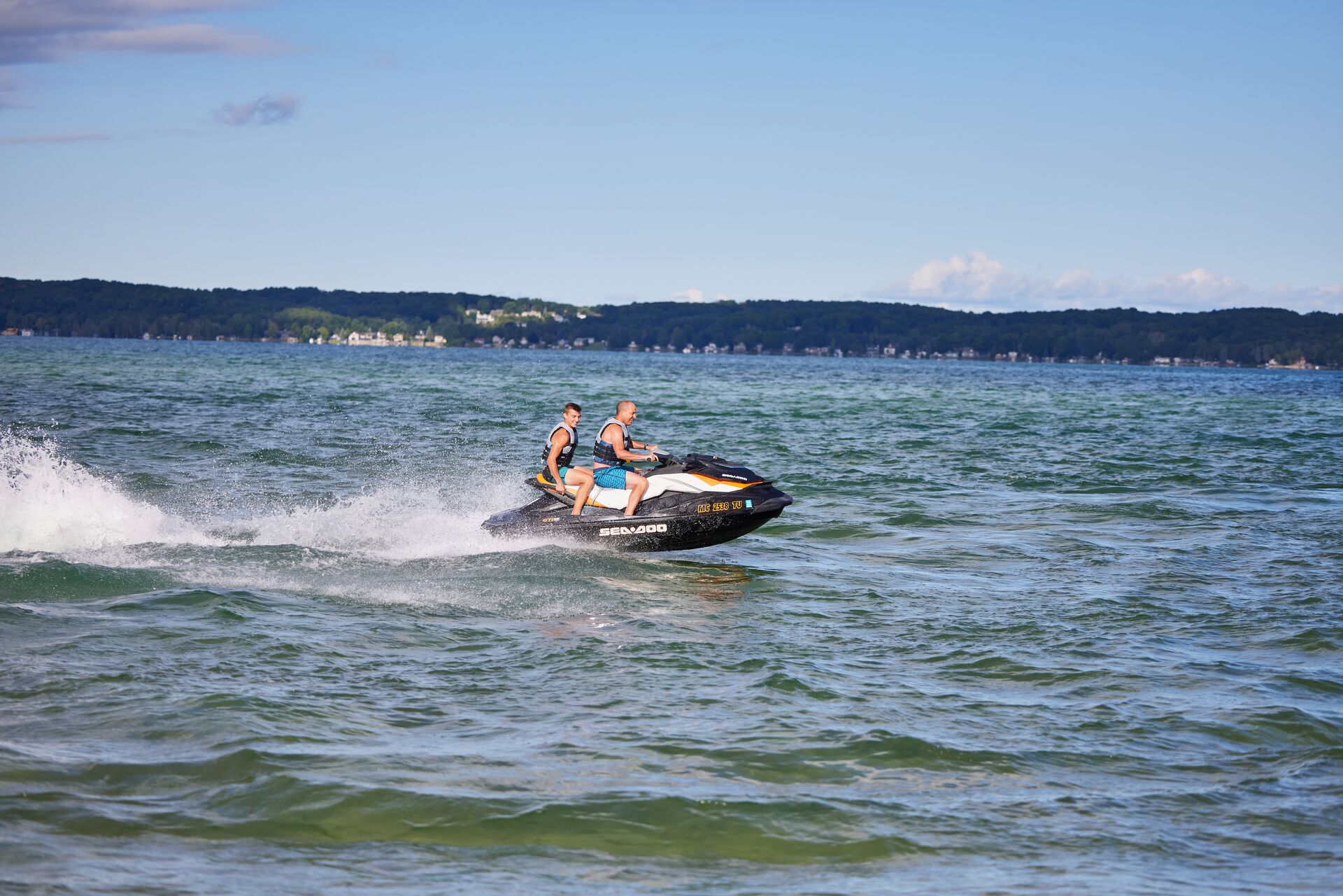 Two people riding a personal watercraft on a lake. 